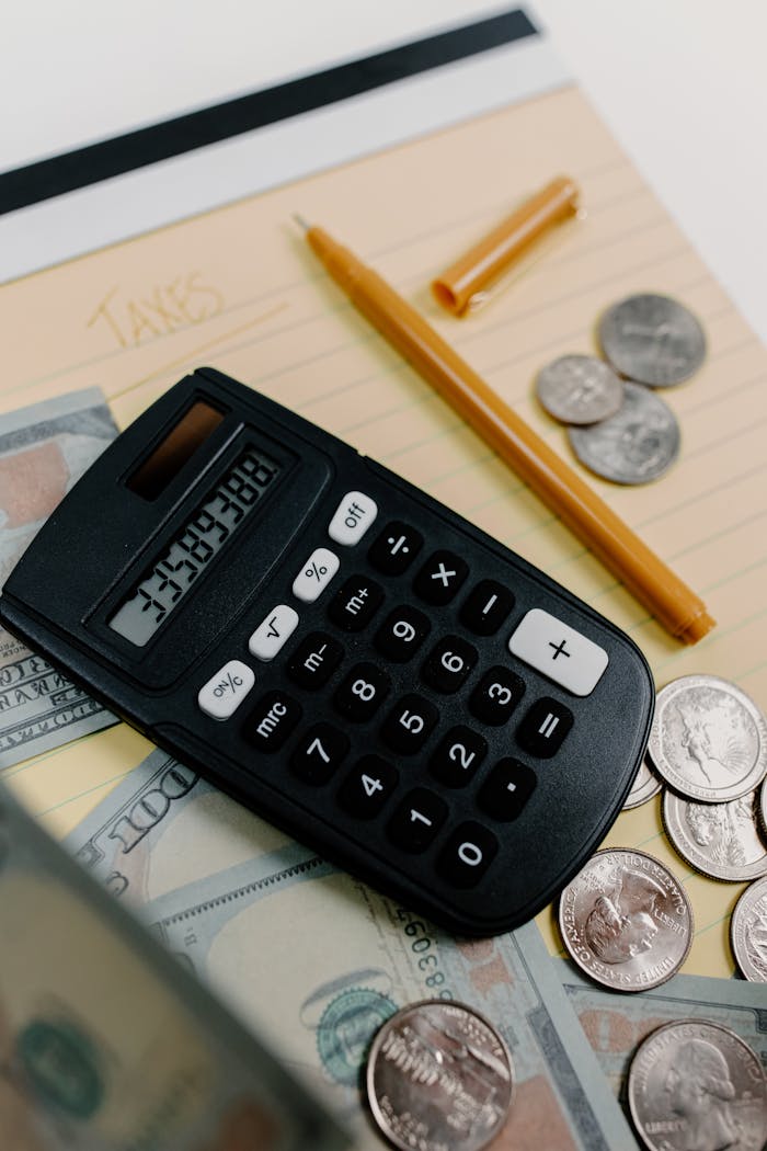 Close-up of a calculator, cash, and coins on a desk with a notepad and pen for financial planning.